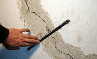 A wall with a large crack is being inspected by a professional in Tulsa, OK